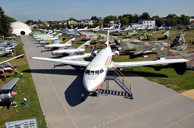 Zdjęcie przedstawia rożne samoloty i helikoptery stojące obok siebie w przestrzeni muzeum.