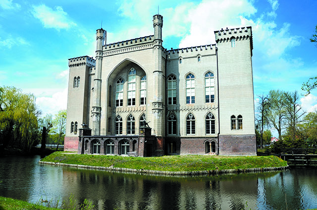 Zdjęcie przedstawia fasadę zamku w Kórniku otoczonego wypełnioną wodą fosą.