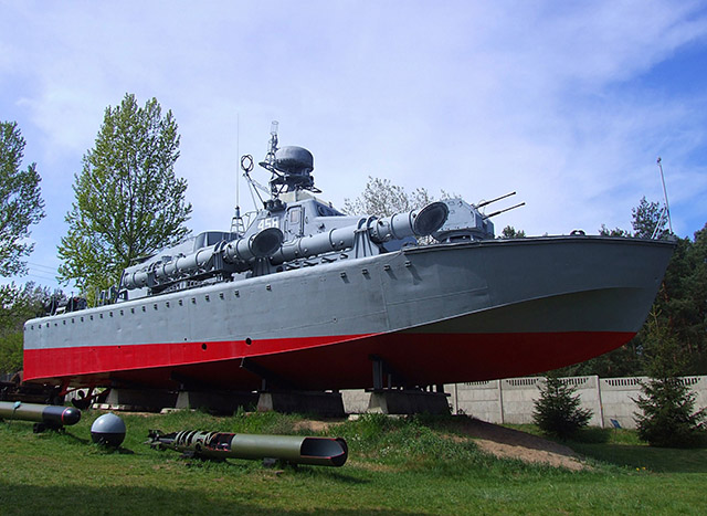 Zdjęcie przedstawia model okrętu wojennego w pomniejszeniu, stojącego na podstawach