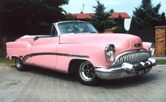 Zdjęcie przedstawia stary, różowy samochód bez dachu marki Cadillac.